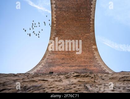 Vertikale alte Eisenbahnbogenbrücke aus Stein und Ziegel, die vom Boden hoch oben in den blauen Himmel blickt. Taubenvögel ziehen ab Stockfoto