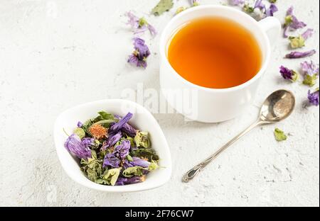 Kräutertee in einer weißen Schüssel und in einem weißen tasse und einen Teelöffel auf einem hellgrauen Tisch Stockfoto