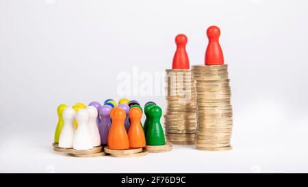 Zwei große Münzstapel mit je einer Holzfigur Und mehrere kleine Heftklammern mit vielen Figuren als Symbol für Unlautere Aufteilung des Geldes im W Stockfoto