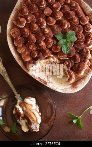 Tiramisu, italienisches Dessert. Hausgemachter Kuchen in einem weißen Tablett mit Marienkäfer und Mascarpone-Creme isoliert auf braunem Hintergrund. Direkt darüber. Stockfoto