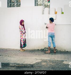 Maskat, Oman, 3. Dezember 2016: Zwei Mädchen an einem Wasserzapfen vor einer Moschee in der Altstadt von Maskat, Oman Stockfoto