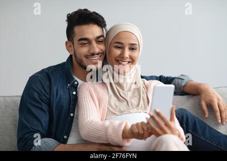 Glücklich erwartet muslimischen Paar Selfie auf dem Smartphone beim Entspannen Zu Hause Stockfoto