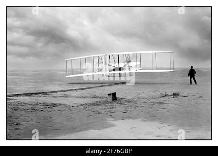 WRIGHT BROTHERS ERSTER MOTORBETRIEBENER FLUG ARCHIV 1900 Wright Brothers machen ersten motorisierten Flug 1903 Kitty Hawk, North Carolina, USA das Amerika-Foto zeigt den ersten motorisierten, kontrollierten, nachhaltigen Flug. Orville Wright an den Bedienelementen der Maschine, gestreckt auf dem unteren Flügel mit Hüften in der Wiege liegend, die den Wing-Warping-Mechanismus betätigte. Wilbur Wright läuft mit, um die Maschine zu balancieren, hat gerade seinen Halt an der nach vorne aufrechten Seite des rechten Flügels freigegeben. Hinter der Maschine sind die Startschiene, die Flügelstütze, eine Spulenbox und andere Elemente, die für die Flugvorbereitung benötigt werden, sichtbar. Stockfoto