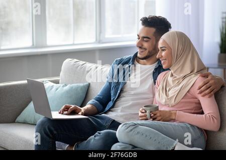 Entspannter arabischer Mann und Frau, die sich einen Film auf dem Laptop ansehen Stockfoto