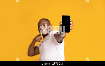 Fröhlicher afroamerikanischer Mann mittleren Alters in weißem T-Shirt Zeigt den Finger am Telefon an Stockfoto