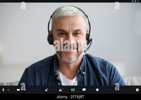 Lächelnder älterer Mann, der eine Videokonferenz mit einem Headset führt Stockfoto