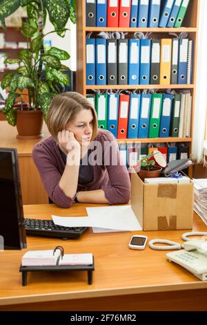 Verärgert entlassene junge Angestellte mit verpackter Kiste am Arbeitsplatz am letzten Arbeitstag, frustrierte Büroangestellte, die sich nach der Entlassung auf die Abreise vorbereitete Stockfoto