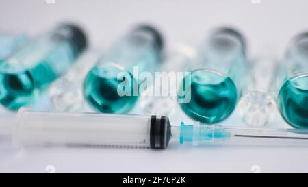 Fläschchen-Impfstoff, Draufsicht auf Glasampullen mit transparenter und blauer Flüssigkeit, eine Spritze liegt nahe auf weißem Hintergrund, globales Impfkonzept Stockfoto