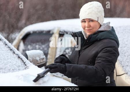 Frau, die im Winter Schnee aus dem Auto mit schwarzer Bürste entfernt Saison Stockfoto