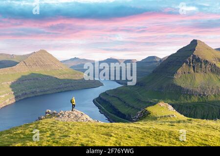 Einsamer Tourist in gelber Jacke mit Blick auf majestätische Fjorde von Funningur, Insel Eysturoy, Färöer. Landschaftsfotografie Stockfoto