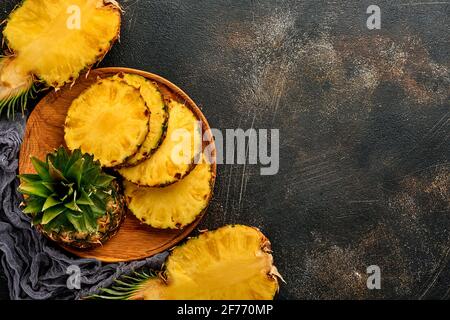 Geschnittene reife Ananas auf dunkelbraunem Steingrund. Tropische Früchte. Draufsicht. Freier Speicherplatz für Text. Modell. Stockfoto