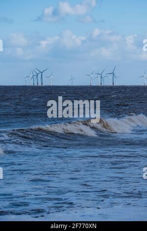 Die Wellenmacht der Nordsee auf der Lincolnshire Küste mit Windturbinen in der Ferne, die die Bereitstellung ermöglichen Erneuerbare und nachhaltige Energie Stockfoto