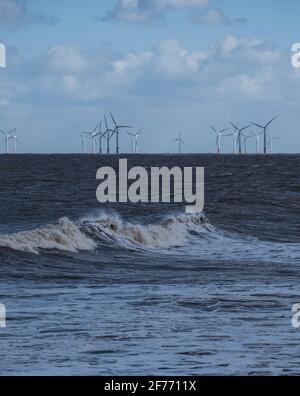 Die Wellenmacht der Nordsee auf der Lincolnshire Küste mit Windturbinen in der Ferne, die die Bereitstellung ermöglichen Erneuerbare und nachhaltige Energie Stockfoto