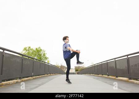 Ein junger Athlet trainiert auf der Straße, indem er sich dehnt Seine Beine Stockfoto