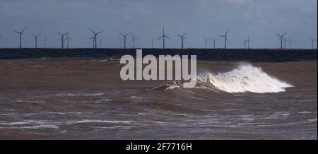 Die Wellenmacht der Nordsee auf der Lincolnshire Küste mit Windturbinen in der Ferne, die die Bereitstellung ermöglichen Erneuerbare und nachhaltige Energie Stockfoto