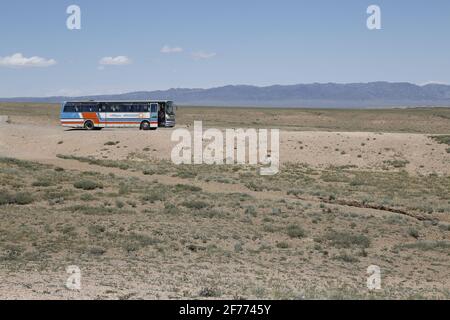Ein Bus steht allein in einer leeren, wilden Wüstenlandschaft; Hügel im Hintergrund; keine Menschen oder Zivilisation sichtbar; er sieht heiß und trocken aus. Stockfoto