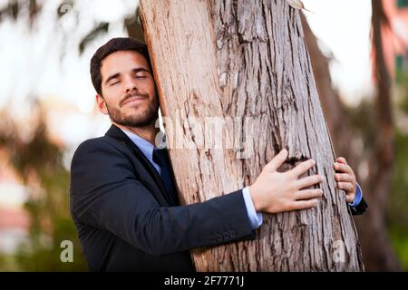 Ein Geschäftsmann umarmt einen Baumstamm Stockfoto