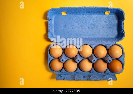 Frische Eier in und aus dem blauen Karton isoliert Auf gelbem Hintergrund Stockfoto