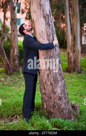 Ein Geschäftsmann umarmt einen Baumstamm Stockfoto