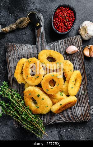 Frittierte Tintenfisch Calamari Ringe paniert auf einem Schneidebrett. Schwarzer Hintergrund. Draufsicht. Stockfoto