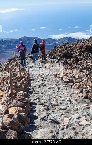 Familie aus drei Personen, die winddichtige Jacken mit Kapuze tragen, wandern auf der alpinen Wanderroute im Vulkan Teide, auf den Kanarischen Inseln, Spanien, Europa Stockfoto