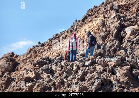 Drei Wanderer steigen bei sonnigem und klarem Wetter auf einem Steinweg zwischen den Lavahaufen hoch in den Bergen hinab. Der Vulkan Teide, Teneriffa, Kanarische Inseln Stockfoto