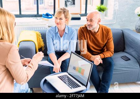 Glückliches Paar, das mit ihrem Finanzberater kommuniziert, während es zu Hause im Wohnzimmer sitzt. Stockfoto