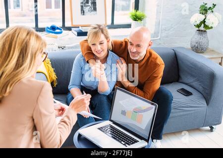 Glückliches Paar, das mit ihrem Finanzberater kommuniziert, während es zu Hause im Wohnzimmer sitzt. Stockfoto