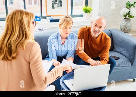 Glückliches Paar, das mit ihrem Finanzberater kommuniziert, während es zu Hause im Wohnzimmer sitzt. Stockfoto