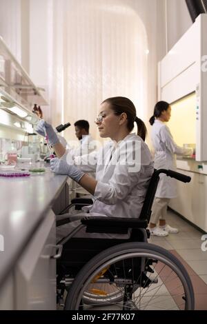 Junge behinderte Wissenschaftlerin, die am Tisch im Labor arbeitet Stockfoto