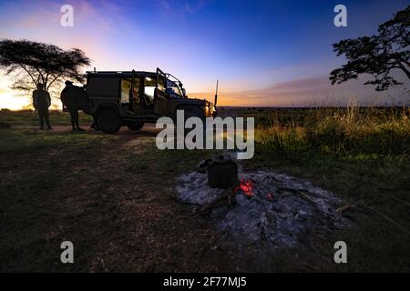 Tansania, WMA (Wildtierschutzgebiet) von Randilen, Monduli-Bezirk, Arusha-Region, Lagerfeuer in der Dämmerung, 4x4 im Hintergrund Stockfoto