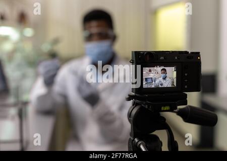 Afrikanischer junger Wissenschaftler hält Reagenzglas mit Flüssigkeit und sieht aus Vor der Kamera nahm er ein Video für seinen Blog auf Stockfoto