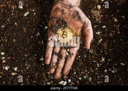 Eine goldene Bitcoin auf der schmutzigen Hand eines Bergarbeiters. Metapher für den Abbau von BTC und Kryptowährungen. Digitales Business und dezentrales Finanzkonzept Stockfoto