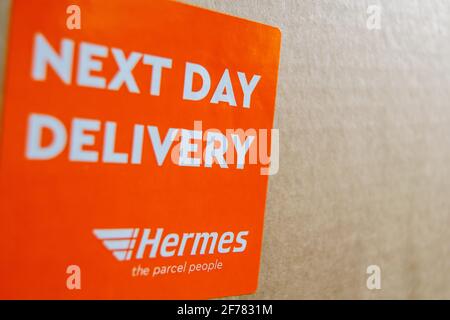 Thame, UK 25 Mar 2021: Orange Lieferung am nächsten Tag Hermes-Etikett auf dem Karton, Logo-Aufkleber auf einem Paket, schneller Kurierdienst geliefert, groß Stockfoto