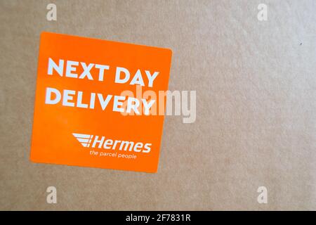 Thame, UK 25 Mar 2021: Orange Lieferung am nächsten Tag Hermes-Etikett auf dem Karton, Logo-Aufkleber auf einem Paket, schneller Kurierdienst geliefert, groß Stockfoto