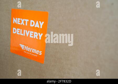 Thame, UK 25 Mar 2021: Orange Lieferung am nächsten Tag Hermes-Etikett auf dem Karton, Logo-Aufkleber auf einem Paket, schneller Kurierdienst geliefert, groß Stockfoto