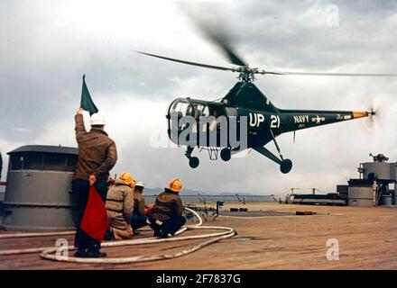 USS New Jersey (BB-62) EIN Sikorsky HO3S-1 Hubschrauber der Staffel HU-1 hebt vom Nachdeck des Schlachtschiffes ab, während sie vor Korea operieren musste. Die hochgelobte grüne Flagge bedeutet, dass der Pilot die Startgenehmigung hat. Die Crash-Crew, in gelben Helmen, steht mit Feuerwehrschläuchen bereit. Das Foto datiert vom 14. April 1953. Fotograf ist LT. R.C. Timm. Offizielles US-Navy-Foto Stockfoto