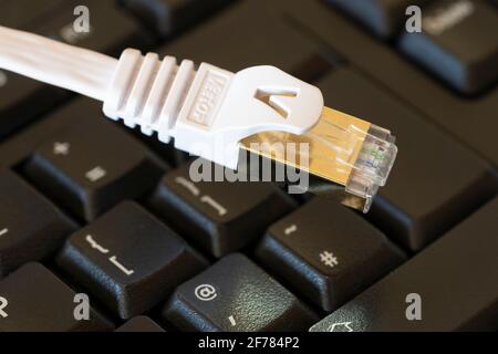 Nahaufnahme eines weißen ethernet-Kabels (Internet) auf einer schwarzen Tastatur. Konzept: internetzugang, Breitband, Internetausfall, Hacking, digital Stockfoto