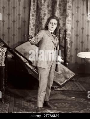 1910ER-1920ER-JAHRE ERSCHRECKTE SCHAUSPIELERIN FRAU ALS MANN IN DREI GEKLEIDET PIECE SUIT ZEIGT EINE WAFFE STUMMFILM NOCH - ASPHAL211 ASP001 HARS B&W-FILME BIZARRE DARSTELLENDE KÜNSTE HUMORVOLLER, SELTSAMER PERFORMER SCHUTZ MELODRAM GROTESKE ZANY KOMISCHEN REVOLVER UNKONVENTIONELLE VERKLEIDUNG ENTERTAINER BERUFE VERÄNGSTIGTE STUMME SCHAUSPIELER COMEDY DRAMA ABGEDREHTE IDIOSYNKRATISCHE FILM-PUBLICITY IMMER NOCH THEATRALISCHE AMÜSANT EXZENTRISCHE ENTERTAINER SCHUSSWAFFEN GESCHLECHT MITTLEREN ERWACHSENEN MITTLEREN ERWACHSENEN MANN MITTLEREN ERWACHSENEN FRAU FILM IMMER NOCH DARSTELLER SCHWARZ-WEISS KAUKASISCH ETHNISCHE ZUGEHÖRIGKEIT UNBERECHENBAR ALTMODISCH EMPÖREND Stockfoto