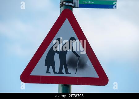 Ältere Menschen überqueren dreieckiges Warnschild. Stockfoto