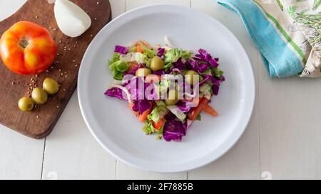 Flacher Blick auf einen frischen salat im mediterranen Stil, der auf einem weißen Tisch platziert wird Stockfoto