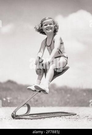 LÄCHELNDES MÄDCHEN AUS DEN 1930ER JAHREN, DAS AUF EINEM METALLFEDERSPIELZEUG SCHAUKELND HÜPFT HOBBY PFERD - J6019 HAR001 HARS SOMMERLICHER BLICKKONTAKT HUMORVOLL GLÜCK FRÖHLICH HOBBY AUFREGUNG LOW-ANGLE ERHOLUNG KOMISCH LÄCHELT KOMÖDIE FRÖHLICHES WACHSTUM JUVENILE JAHRESZEIT SCHWARZ-WEISS KAUKASISCHEN ETHNIZITÄT HAR001 ALTMODISCH Stockfoto