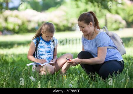 Mutter, die ihrer Tochter dabei half, die Natur zu skizzieren, eine Erwachsene Frau und ein Mädchen vor dem Teenager, das im grünen Gras sitzt Stockfoto