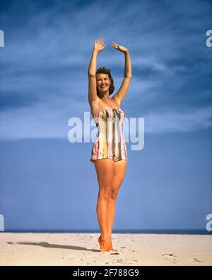 LÄCHELNDE FRAU AUS DEN 1950ER JAHREN IN EINEM STÜCK VERTIKAL GESTREIFTEN BADEN ANZUG POSIERT AM STRAND ARME ANGEHOBEN FT LAUDERDALE FLORIDA USA - KB32336 HAR001 HARS KOPIEREN RAUM IN VOLLER LÄNGE DAMEN PERSONEN AUGE KONTAKTIEREN SIE BRUNETTE ZEIT ABSEITS DER KÜSTE FRÖHLICHE STILE REISE KURZURLAUB ERHOLUNG STRÄNDE URLAUB BERUFE POSIEREN LÄCHELT FRÖHLICH SANDIG STILVOLLE MODE MODELLIERUNG POSE TAN GEBRÄUNTE FERIEN JUNGE ERWACHSENE FRAU KAUKASISCHE ETHNIE HAR001 ALTMODISCH Stockfoto