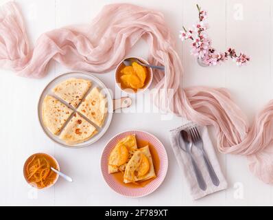 Pancakes Suzette, traditionelles französisches Dessert. Pfannkuchen mit Orangen. Weißer Holztisch. Draufsicht. Stockfoto