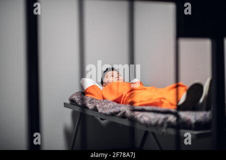 Asiatischer Mörder, der zu einer langen Gefängnisstrafe verurteilt wurde, liegt auf einer Koje in einer Hochsicherheitskolonie in einer Zelle hinter Gittern. Stockfoto