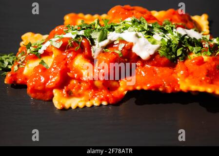 Vier mit Käse gefüllte Ravioli in Tomaten- und Basilikumsoße auf dem schwarzen Steinteller, einem berühmten Gericht aus der französischen Stadt Nizza Stockfoto