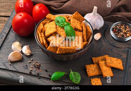 Gesunder Snack, Cracker mit Tomate, Basilikum und Meersalz auf braunem Holzgrund. Seitenansicht, horizontal. Stockfoto