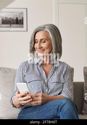 Glückliche ältere ältere Frau genießen mit Handy sitzen auf der Couch zu Hause. Stockfoto