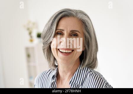 Fröhliche, glückliche, reife Frau aus den 50er Jahren, die lachend die Kamera zu Hause anschaut. Stockfoto